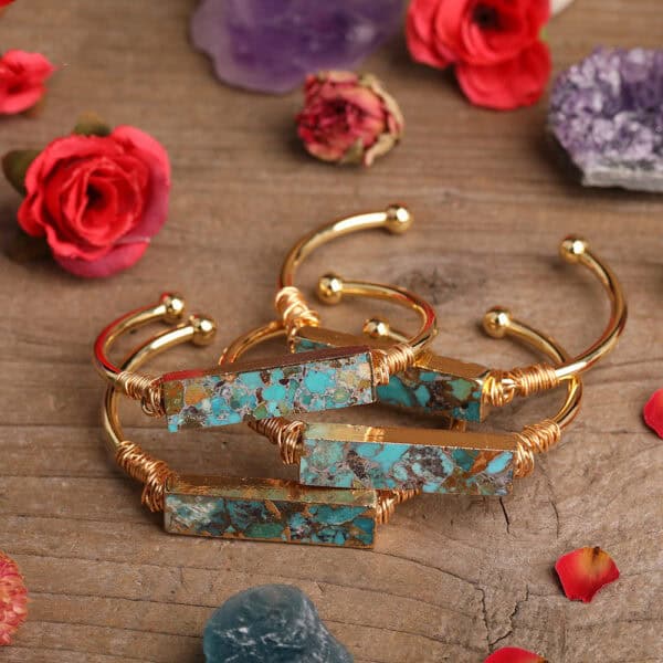 Four Natural Turquoise Inlaid Gemstone Bangles with rectangular stones are arranged on wood, surrounded by red and purple flowers, petals, and decorative stones.
