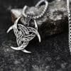 The Triple Horn of Odin Pendant Amulet Necklace features an intricate Celtic knot design with crescent points, inspired by Norse mythology, shown resting on a textured dark stone surface.