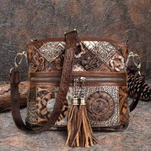 The Cobbler Bohemian Genuine Leather Hand Bag, featuring embossed floral patterns, varied textures, a front zipper pocket, and tassel accents, is displayed on a rustic surface with pinecones and a log in the background.