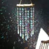 The Multi Strand Suncatcher features crystals and beads hanging from wood, creating vibrant light reflections and rainbows against a dark backdrop.