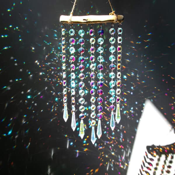 The Multi Strand Suncatcher features crystals and beads hanging from wood, creating vibrant light reflections and rainbows against a dark backdrop.