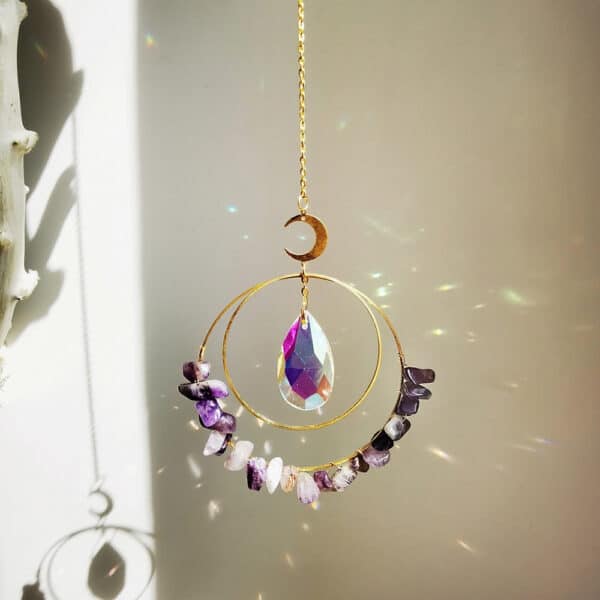 Crystal Moon Suncatchers The Crystal Moon Suncatchers feature a crescent moon, faceted teardrop crystal, and semicircle of amethyst stones on a chain, casting rainbow reflections when sunlight shines through.