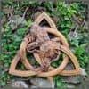 The Odin Ravens Wall Carving features two wooden ravens on intertwined branches within a Celtic triquetra knot, perfect for hanging on any wall adorned with ivy and ferns.