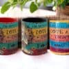 Three Mostly Peace Love N Light & A Little Go F yourself Mugs with floral designs are displayed side by side on a table, with a green plant in the background.