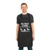 A smiling man wears a black My Meat is 100% Going in Your Mouth BBQ Apron featuring the phrase My Meat is 100% Going in your mouth today! with white graphics of grilling utensils, a flame, and a sausage.
