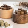 Two round wooden containers, one light and one dark, each hold square wooden blocks in rows. They sit on a white surface alongside the Wooden Essential Oil Diffuser, leaves, and other decorative items.