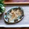 A decorative abalone shell holds small, polished Citrine Tumble Stones—Product: Citrine Tumble Stone small—displayed on a gray cloth with a potted plant partially visible in the corner.
