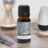 A bottle of Virgo Essential Oil Blend rests on a table beside lavender, an hourglass, and decor. The green label with white and gold accents identifies it as the Virgo Essential Oil Blend.