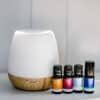 Revive & Thrive Aromatherapy Bundle The Revive & Thrive Aromatherapy Bundle features a white and bamboo essential oil diffuser beside four essential oils with colorful labels, all arranged on a white surface against a light gray background—ideal for enhancing your aromatherapy experience.