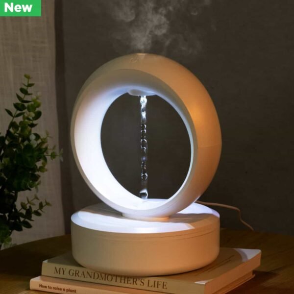 Eclipse Anti-Gravity Diffuser The Eclipse Anti-Gravity Diffuser features water flowing vertically inside a modern white ring. Placed on books beside a small potted plant, soft lighting enhances its calming ambiance.