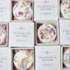 Tranquil Individual Shower Steamers Open white boxes of Tranquil Individual Shower Steamers, each topped with pink and yellow dried flower petals. Arranged in a grid, the packaging reveals both the shower steamer and its product label inside.