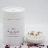 A white cylindrical container labeled Bath Fizzers is placed beside a round bath fizzer with dried flower petals on top, both displayed against a simple white background.