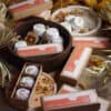 Botanicals Shower Steamers Botanicals Shower Steamers, both boxed and unboxed, are displayed on wooden trays with white bath bombs and topped with dried flowers, surrounded by botanicals, dried leaves, and petals.