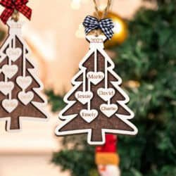 The Custom Christmas Tree Ornament hangs on a tree, featuring heart-shaped spaces labeled Mario, Jessie, David, Emely, and Charlie with a black-and-white bow and 2023 displayed at the top.