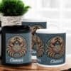 Three Cancer Crab Aboriginal Zodiac Mugs are displayed on a wooden surface, with a green potted plant and a window with white curtains in the background.