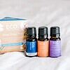 Three small bottles labeled Dream Drops, Sleep Blend, and Lavender rest before a pastel box displaying the product name Deep Sleep Trio Essential Oil 3 Pack, all arranged on a soft white surface.