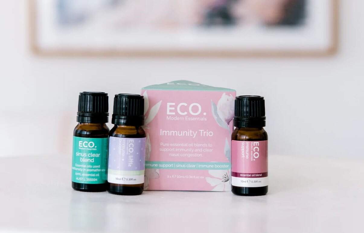 Three small bottles from the Immune Booster Essential Oil Trio Pack are displayed on a white surface, showcasing their immune-boosting blends against a blurred background.
