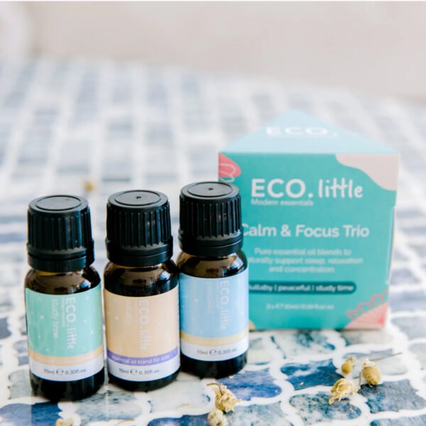 ECO Little Strength Essential Oil Blends For Kids Three small essential oil bottles stand before a blue and teal ECO Little Calm and Focus box on a blue-tiled surface, with dried flowers scattered nearby for a serene touch.