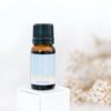 A small amber bottle labeled ECO Little Peaceful Essential Oil Blend with a black cap rests on a white block, with softly blurred white dried flowers in the background.