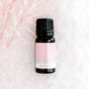 ECO Little Pick Me Up Essential Oil Blend A 10ml bottle of ECO Little Pick Me Up Essential Oil Blend sits on a soft white textured surface, accented by delicate pink-tinted foliage on the left.