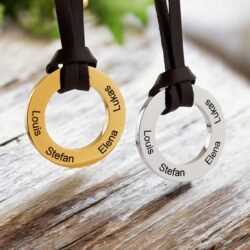 Two Personalised Circle Pendant Necklace on a Leather Strap—one gold, one silver—engraved with Louis, Stefan, Elena, and Lukas rest elegantly on a rustic wooden surface.