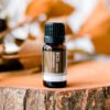 A small amber bottle of Cedarwood Pure Essential Oil sits on a tree stump, with blurred brown and green foliage in the background.