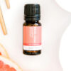 A small amber bottle of Grapefruit Pure Essential Oil rests on a white surface, surrounded by fresh grapefruit slices and two wooden sticks.