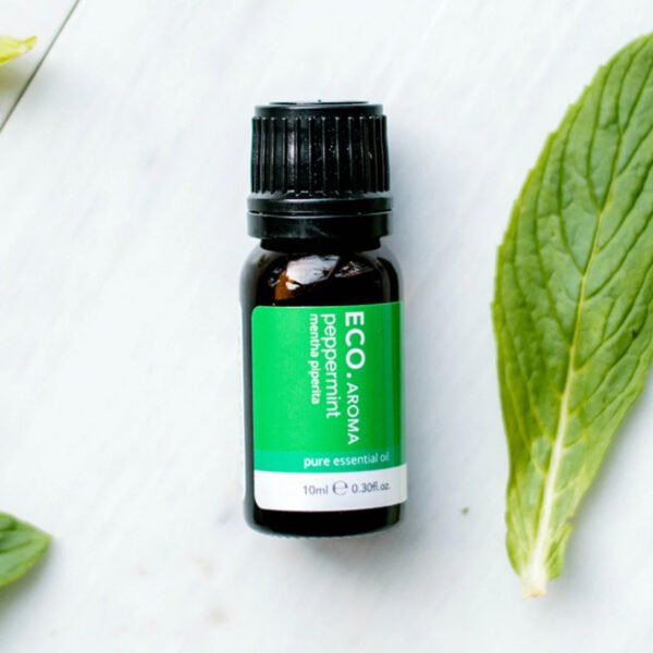 A small dark bottle of Peppermint Pure Essential Oil rests on a light surface, surrounded by fresh green peppermint leaves.