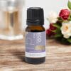 A small amber bottle of Libra Zodiac Essential Oil Blend rests on a wooden surface, with roses and a glass candle holder softly blurred in the background.