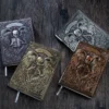 Gothic Angel of Death Notebook Four ornate diaries with embossed covers featuring a skeletal angel holding a sword, displayed on a dark wooden surface. Each diary is a different colour: bronze, gold, silver, and grey.