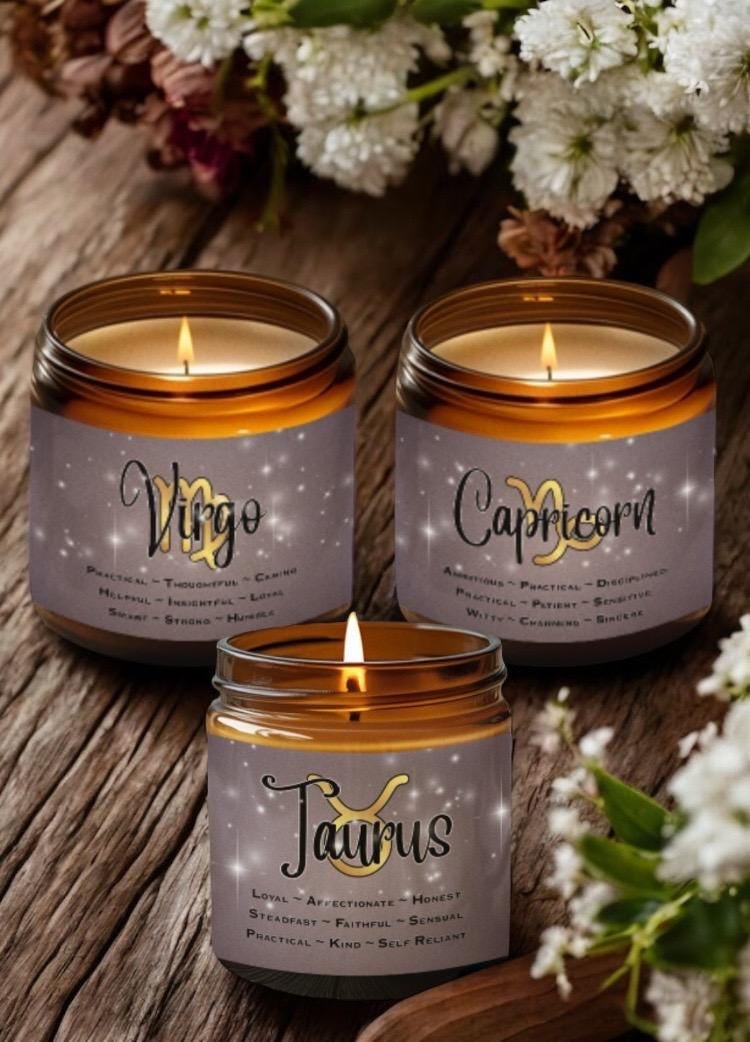 Three lit candles labeled Virgo, Capricorn, and Taurus sit on a wooden surface next to white flowers. Each candle lists personality traits associated with its zodiac sign.