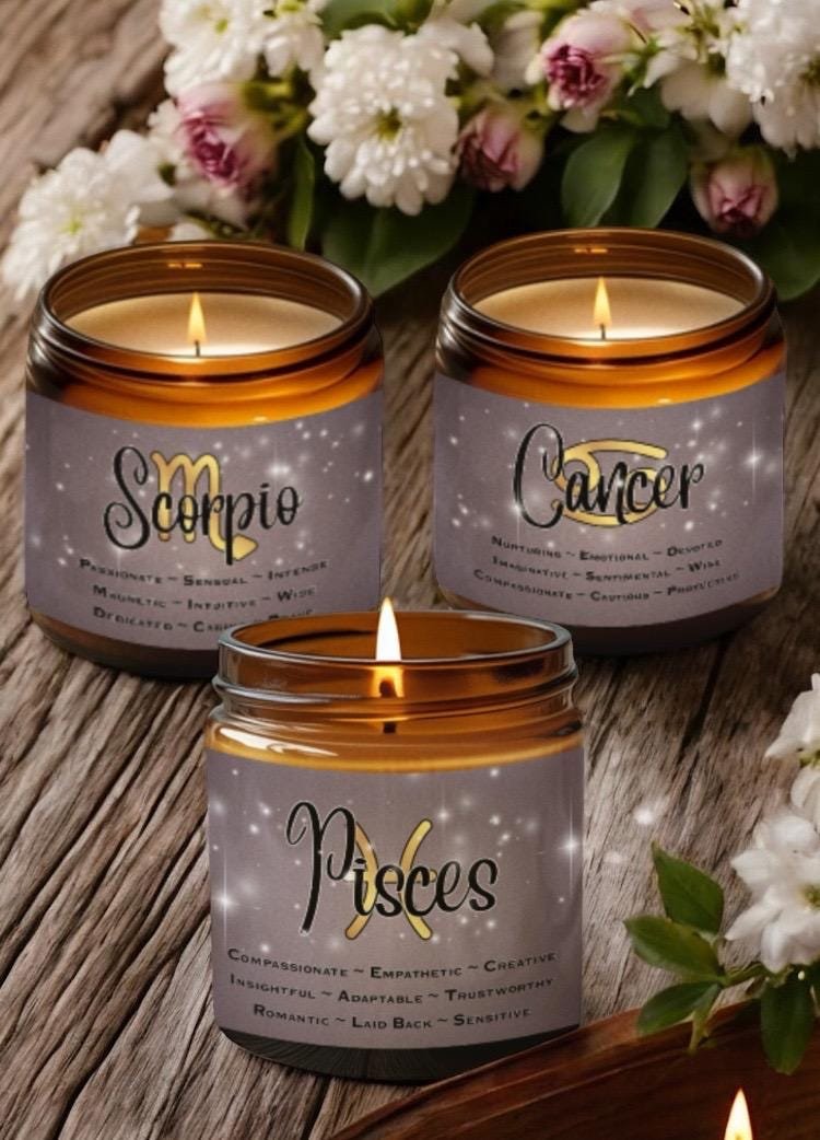 Three zodiac-themed candles labeled Scorpio, Cancer, and Pisces sit on a rustic wooden surface with white and purple flowers nearby. Each candle lists personality traits associated with the sign.