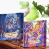 Two colorful illustrated tarot card boxes featuring a woman with flowers in her hair holding Libra scales. The boxes have celestial and floral designs, and display uplifting messages about love, harmony, and dreams.